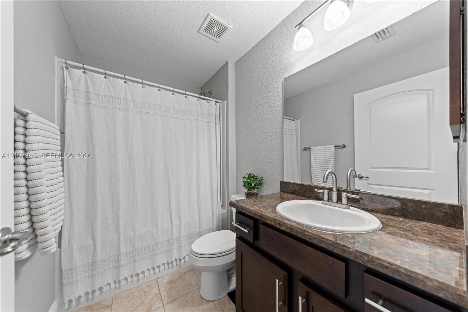 Bathroom featuring a vanity with a dark wood-finish cabinet and stone-surface countertop, an oval under-mount sink, a full-width wall mirror, and a tiled tub-shower combination