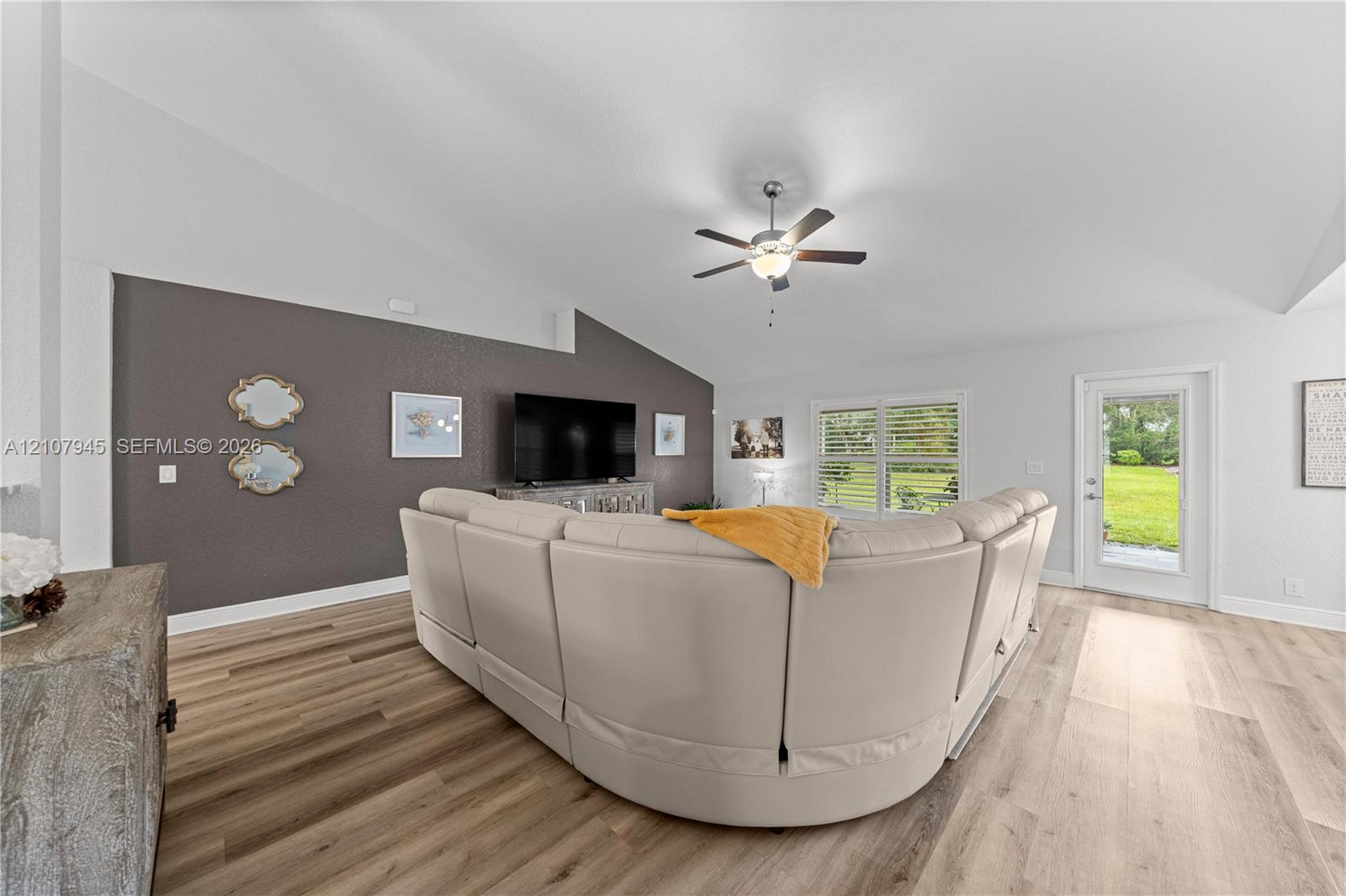 Vaulted ceilings featuring a central light-integrated ceiling fan, wood-finish flooring, and a glass-paneled exterior door