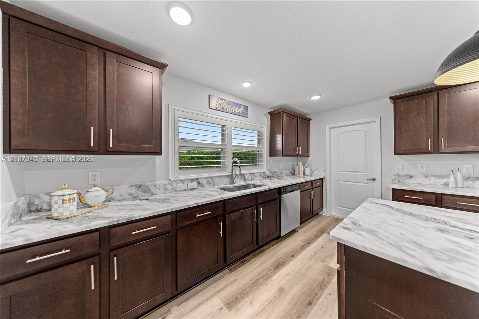 Kitchen featuring dark-finish cabinetry, stone-pattern countertops, stainless steel sink with pull-down faucet, wood-finish flooring, and recessed ceiling lighting
