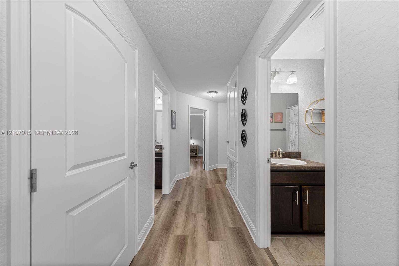 Interior hallway featuring wood-finish flooring, two-panel interior doors, and a bathroom equipped with a vanity, stone-finish countertop, and integrated sink