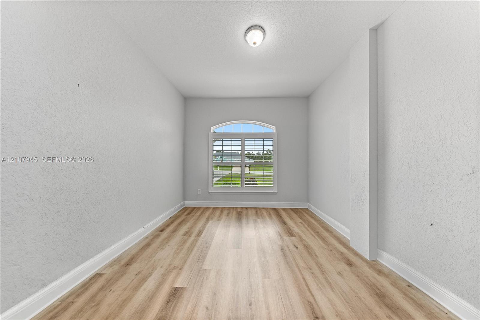 Interior room featuring wood-finish flooring, an arched window with plantation shutters, and a flush-mount ceiling fixture