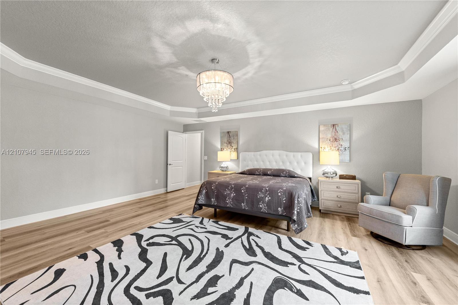 Tray ceiling featuring multi-tiered crown molding, wood-finish flooring, and a crystal chandelier