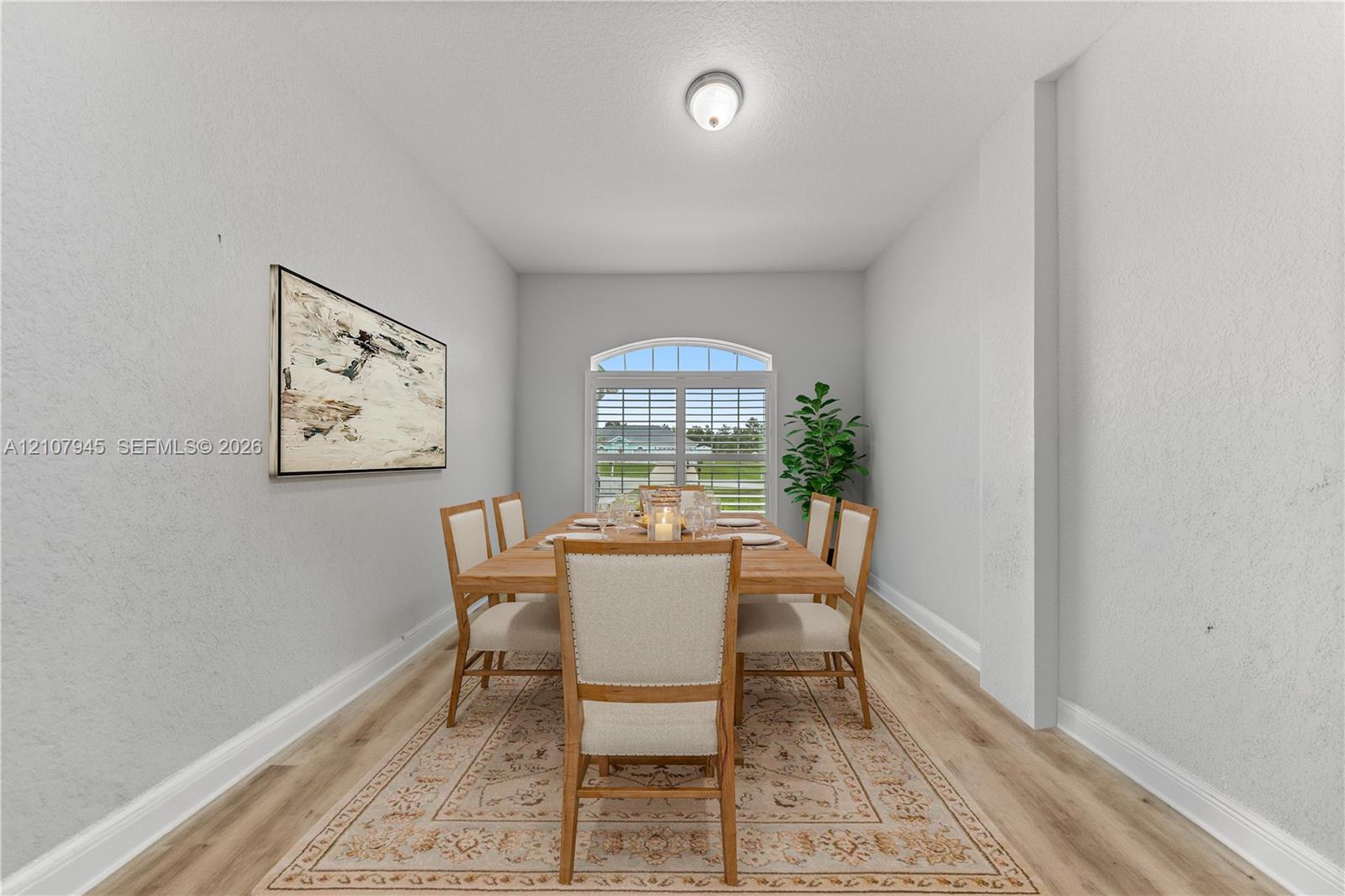 Dining area featuring wood-finish flooring, an arched window with plantation shutters, and a flush-mount ceiling fixture