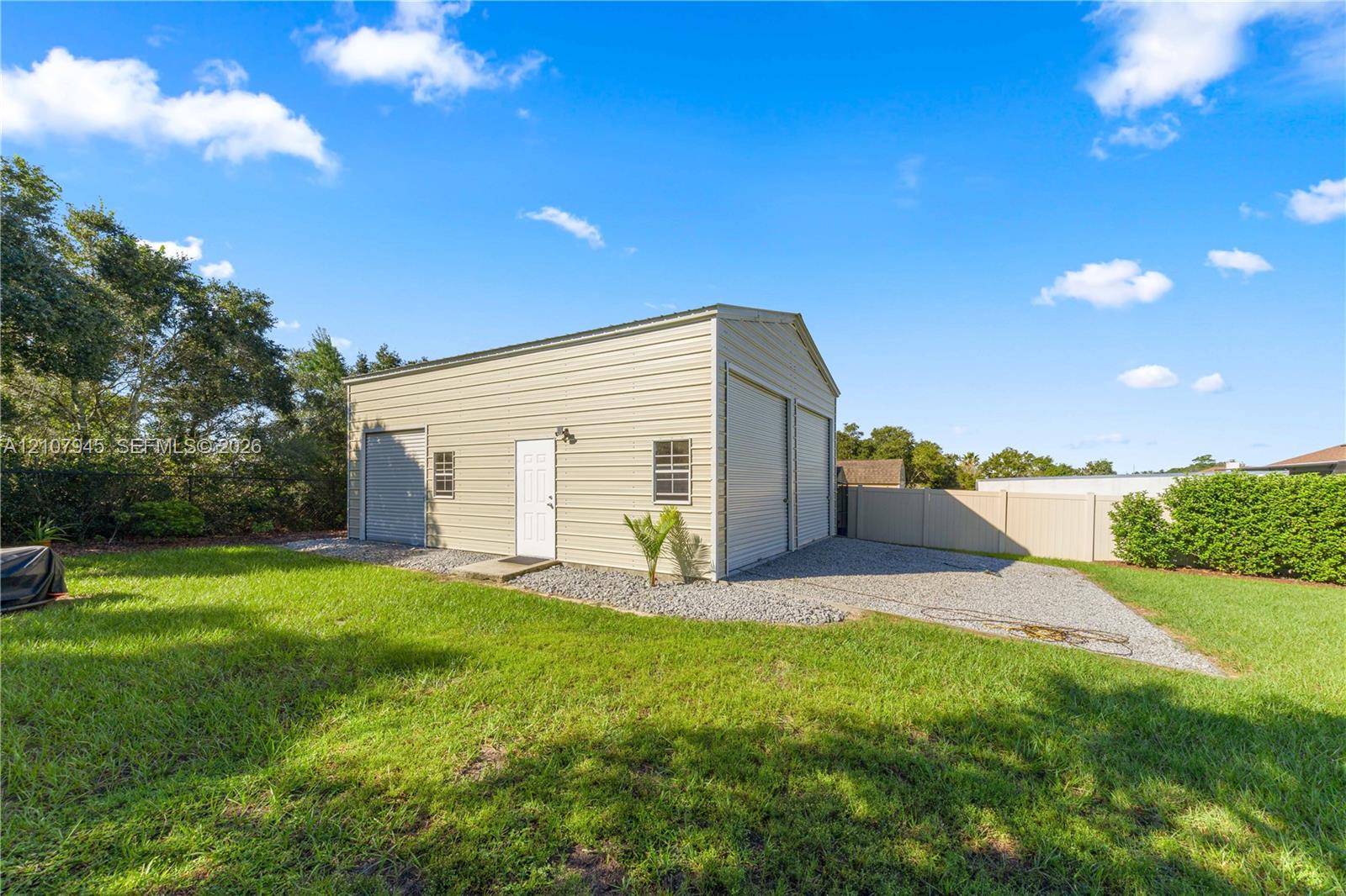Detached metal outbuilding featuring a high-clearance garage door, a side-entry personnel door, dual windows, and an expansive gravel driveway