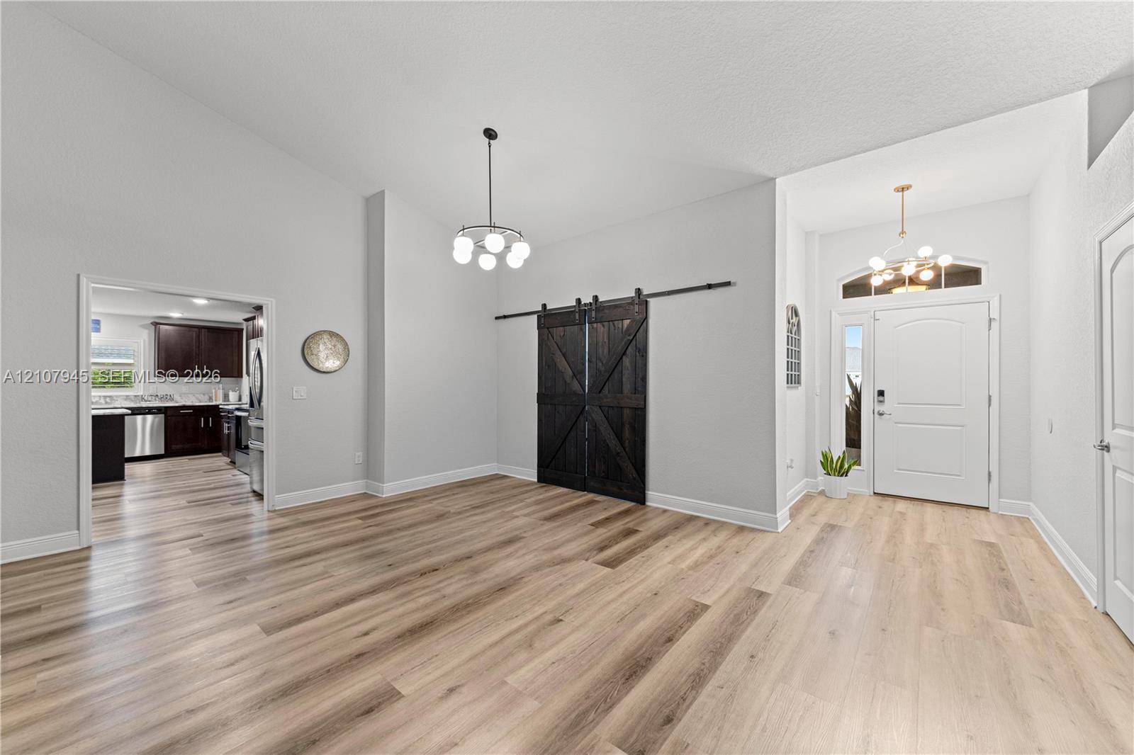 Open-concept area featuring wood-finish flooring, high ceilings, sliding barn-style doors, and decorative pendant lighting