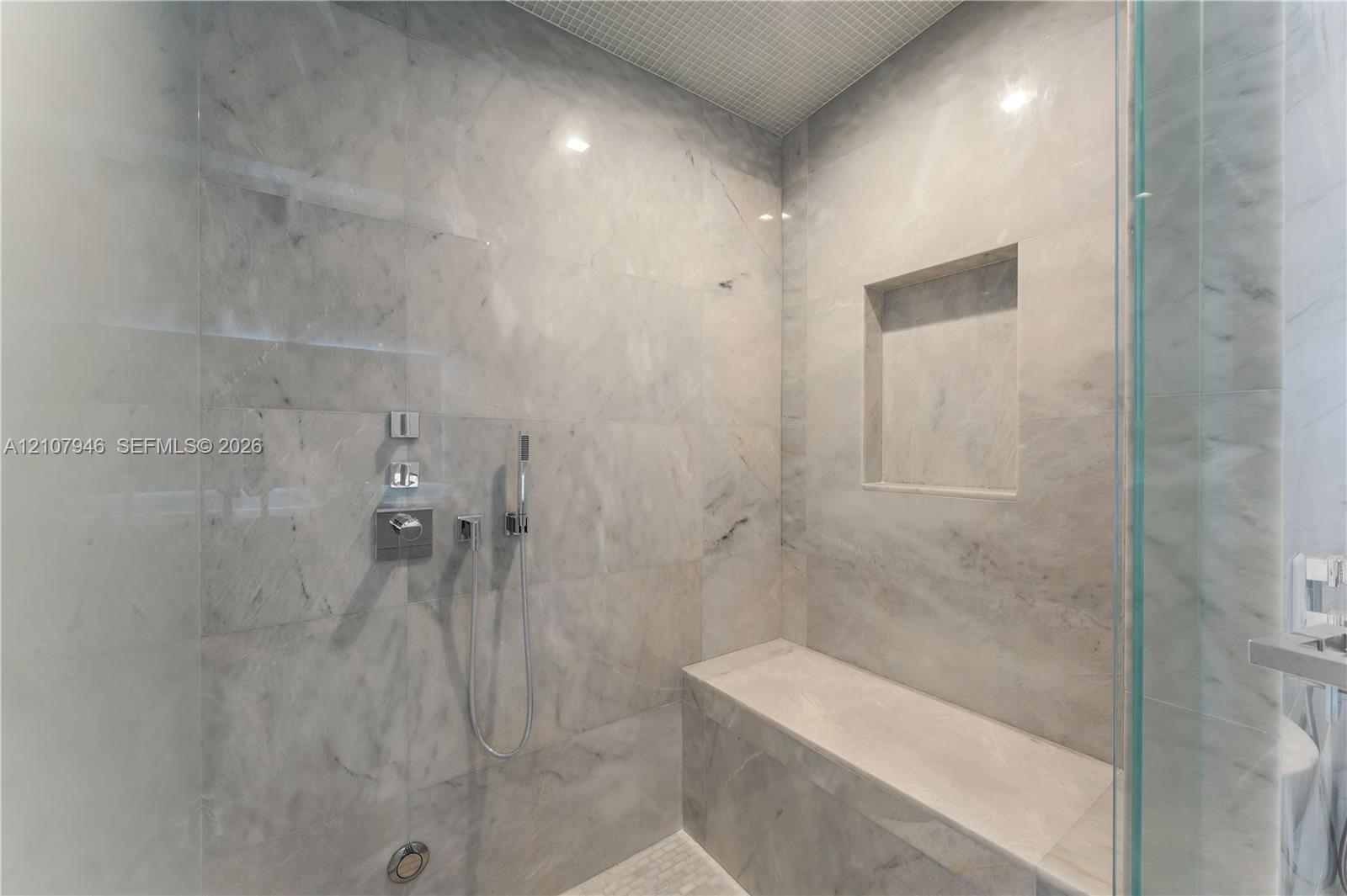 Walk-in shower featuring floor-to-ceiling stone tile, a built-in bench, integrated wall niche, and polished chrome hardware