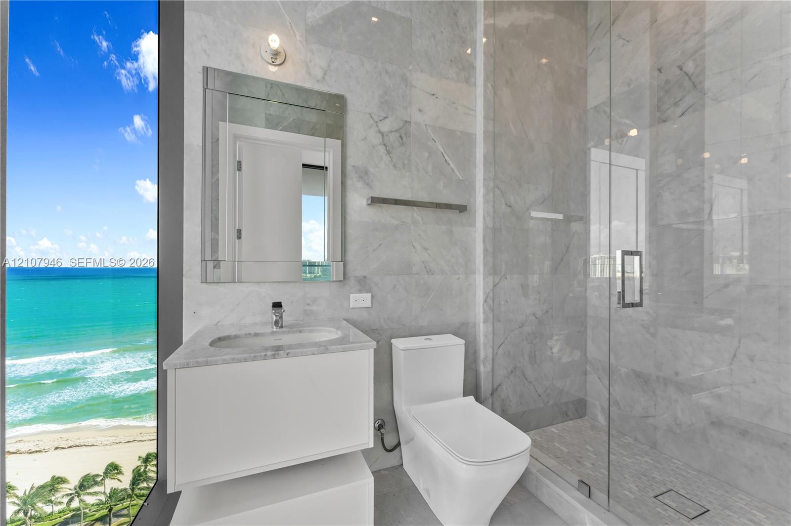 Full-height stone wall tiling, floor-to-ceiling glass paneling, frameless glass shower enclosure, floating vanity with integrated countertop basin, and expansive ocean scenery