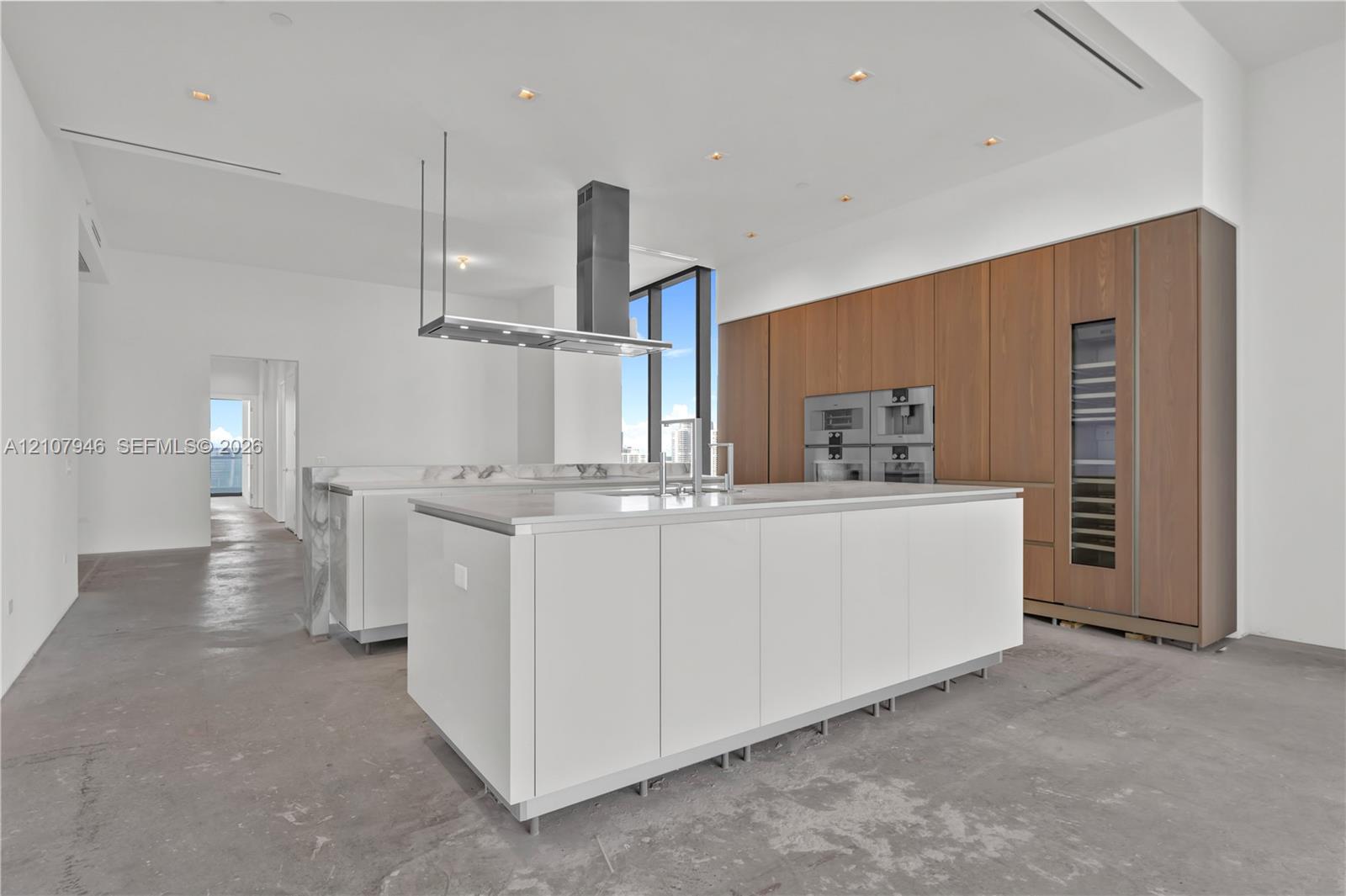 Kitchen featuring a large central island with solid-surface countertop, floor-to-ceiling wood-finish cabinetry, integrated built-in appliances, a stainless steel range hood, and recessed lighting