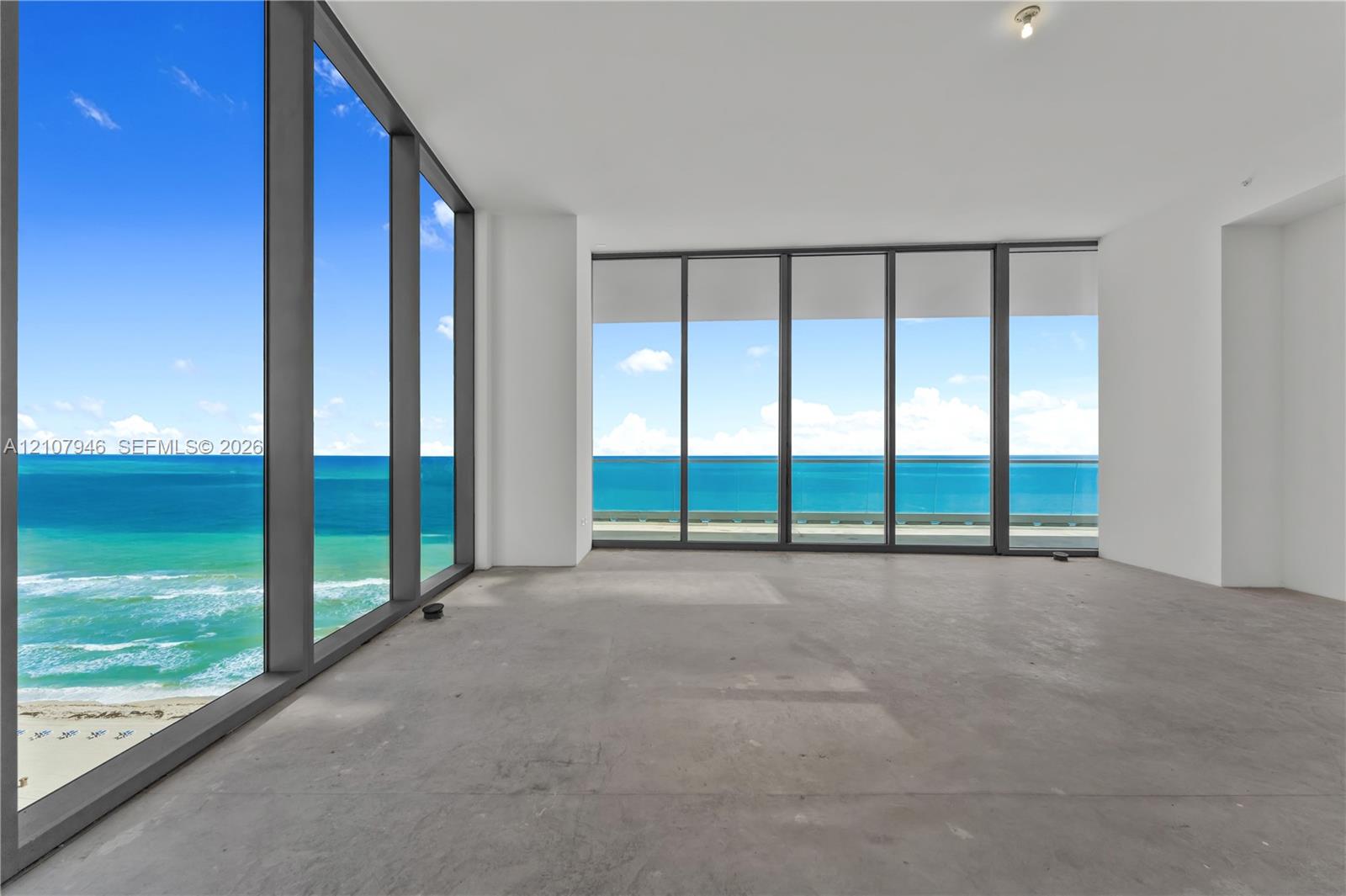 Floor-to-ceiling windows featuring panoramic ocean scenery, concrete flooring, and structural glass railings