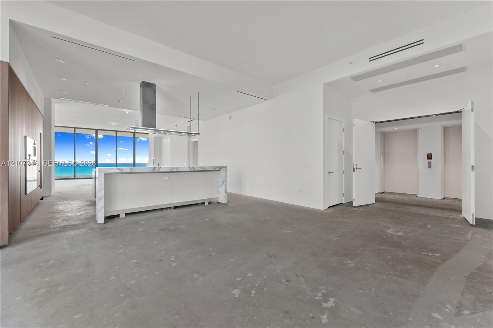 Open concept interior featuring a kitchen island with stone-finish waterfall edges, floor-to-ceiling windows, stainless steel vent hood, and full-height wood-finish cabinetry