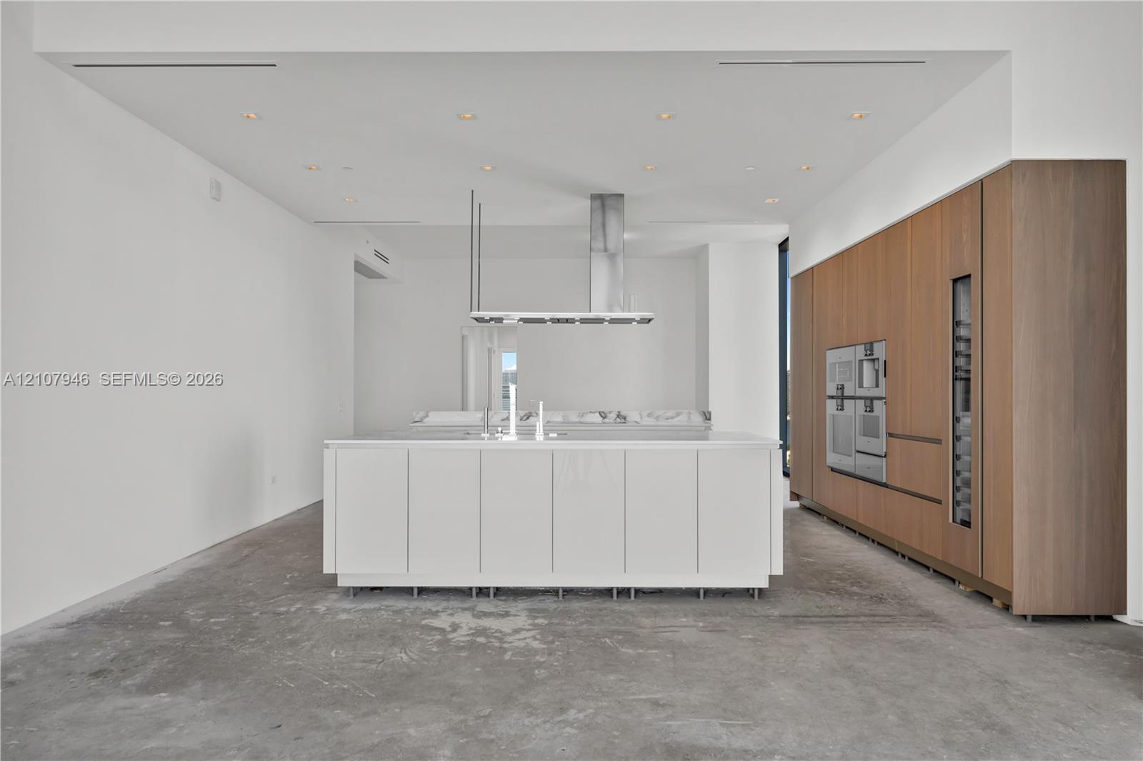 Kitchen featuring a central island with stone countertop, stainless steel overhead range hood, recessed ceiling lighting, built-in wall oven, and wood-finish cabinetry