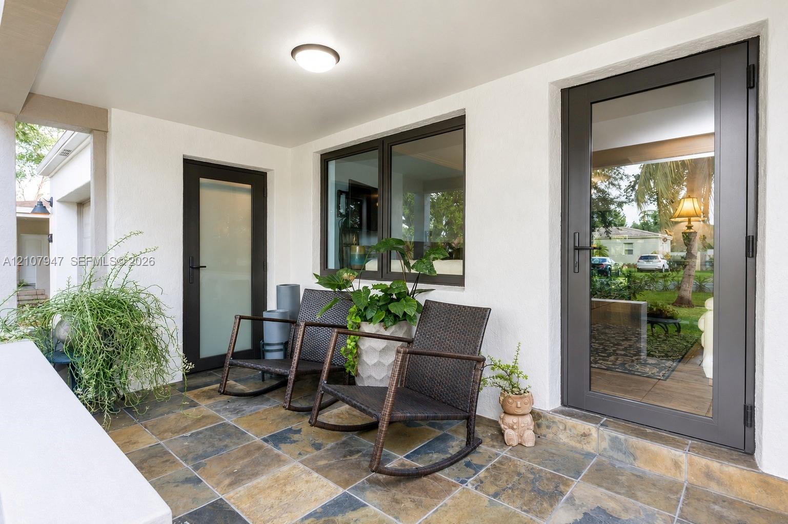 Covered porch featuring multi-tonal slate tile flooring, two full-light glass doors with matte black hardware, and a dual-pane window Covered porch featuring multi-tonal slate tile flooring, two full-light glass doors with matte black hardware, and a dual-pane window