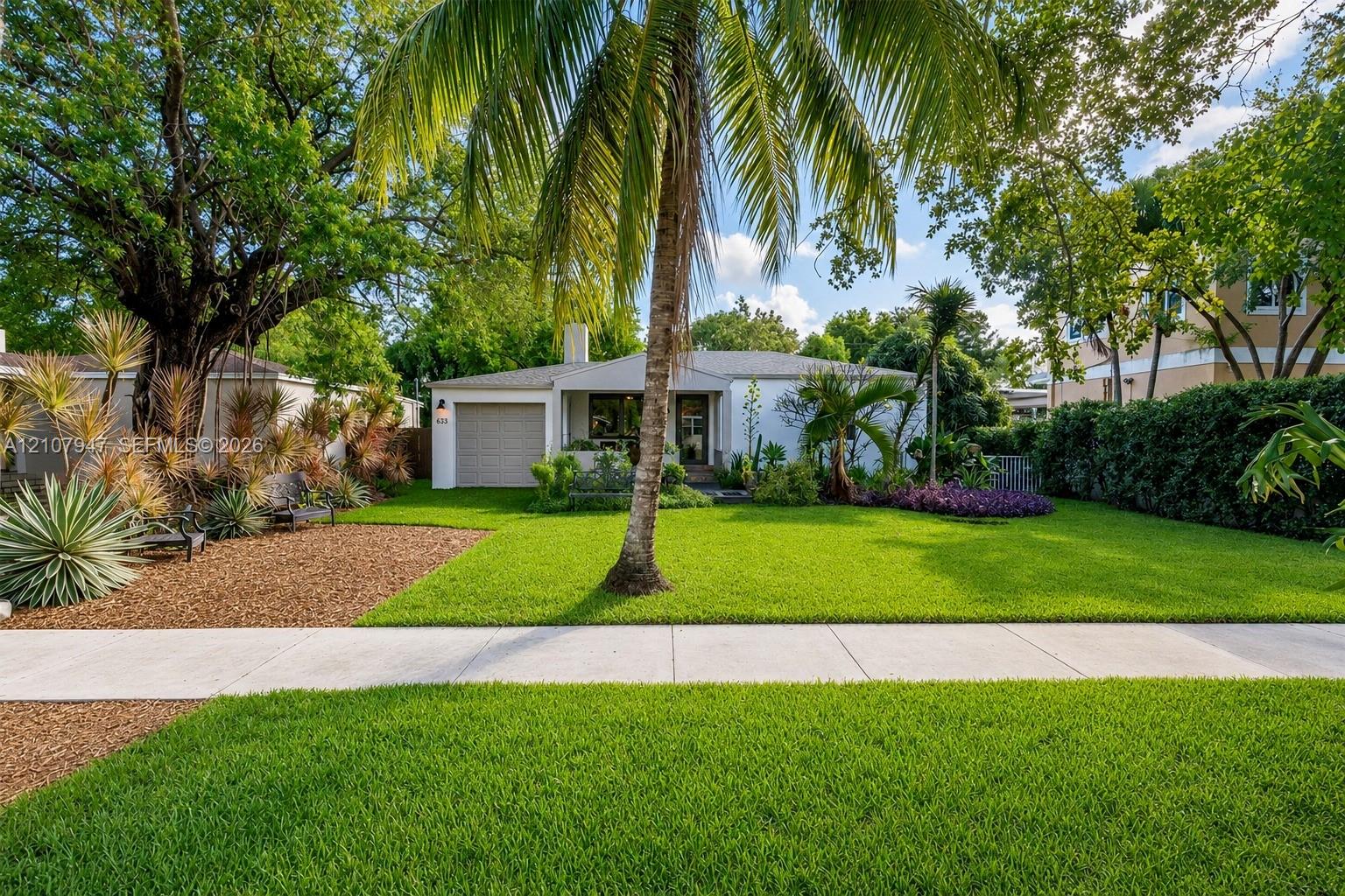 Single-story residence featuring a light-toned exterior, an attached one-car garage, manicured lawn, palm tree, and mature landscaping
