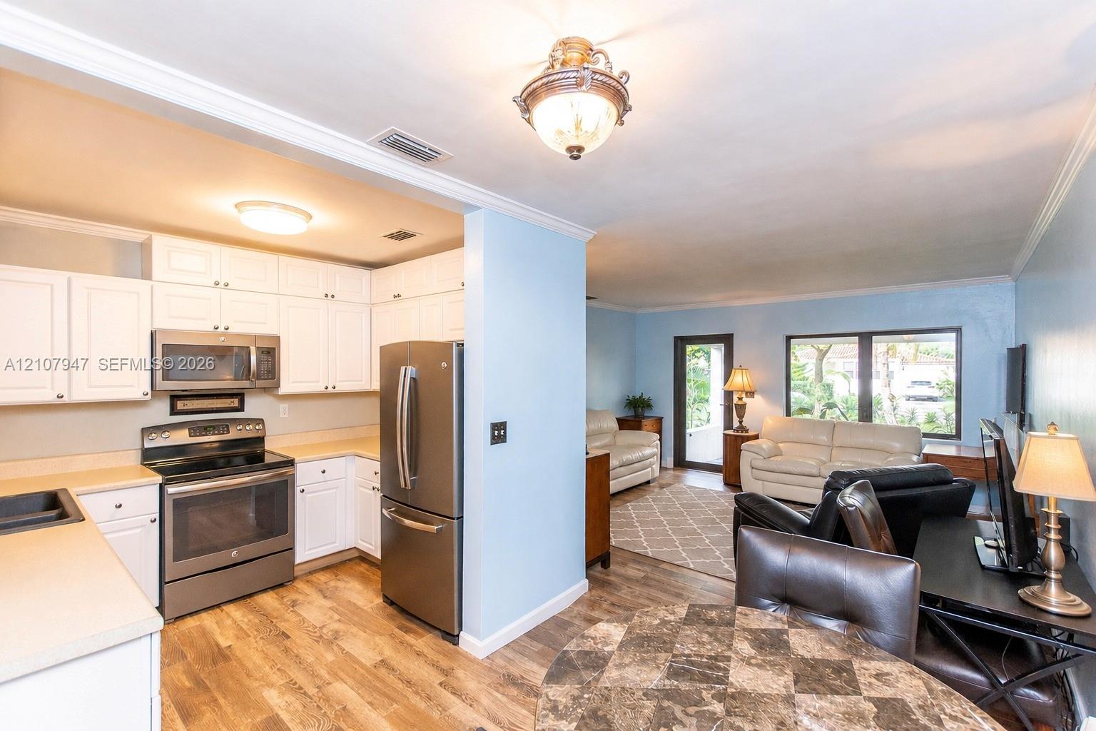 Kitchen featuring white cabinetry, stainless steel appliances, and wood-finish flooring, complemented by a semi-open floor plan with crown molding Kitchen featuring white cabinetry, stainless steel appliances, and wood-finish flooring, complemented by a semi-open floor plan with crown molding