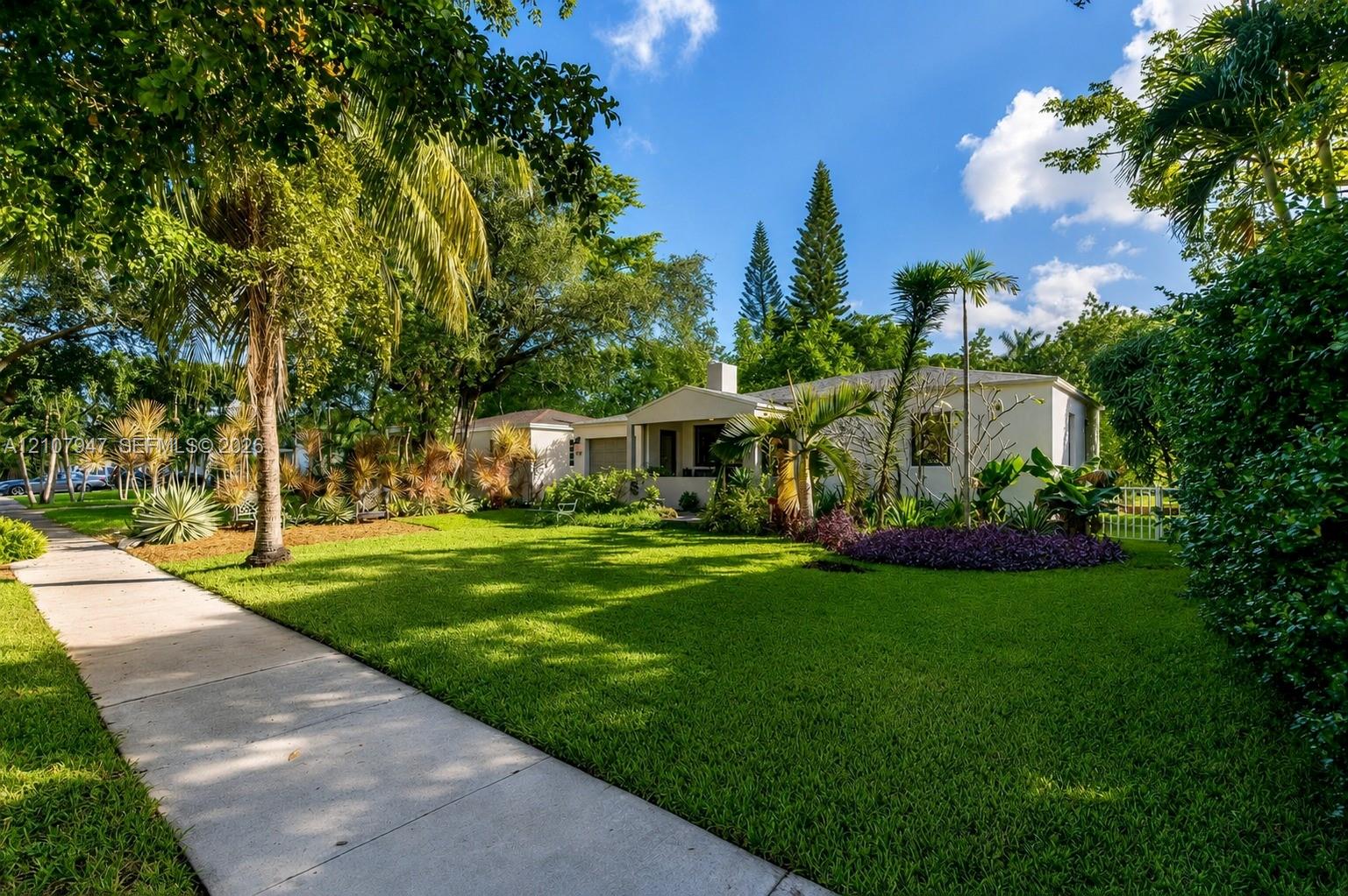 Single-story residence featuring a concrete exterior, covered entryway, manicured lawn, and mature landscaping Single-story residence featuring a concrete exterior, covered entryway, manicured lawn, and mature landscaping
