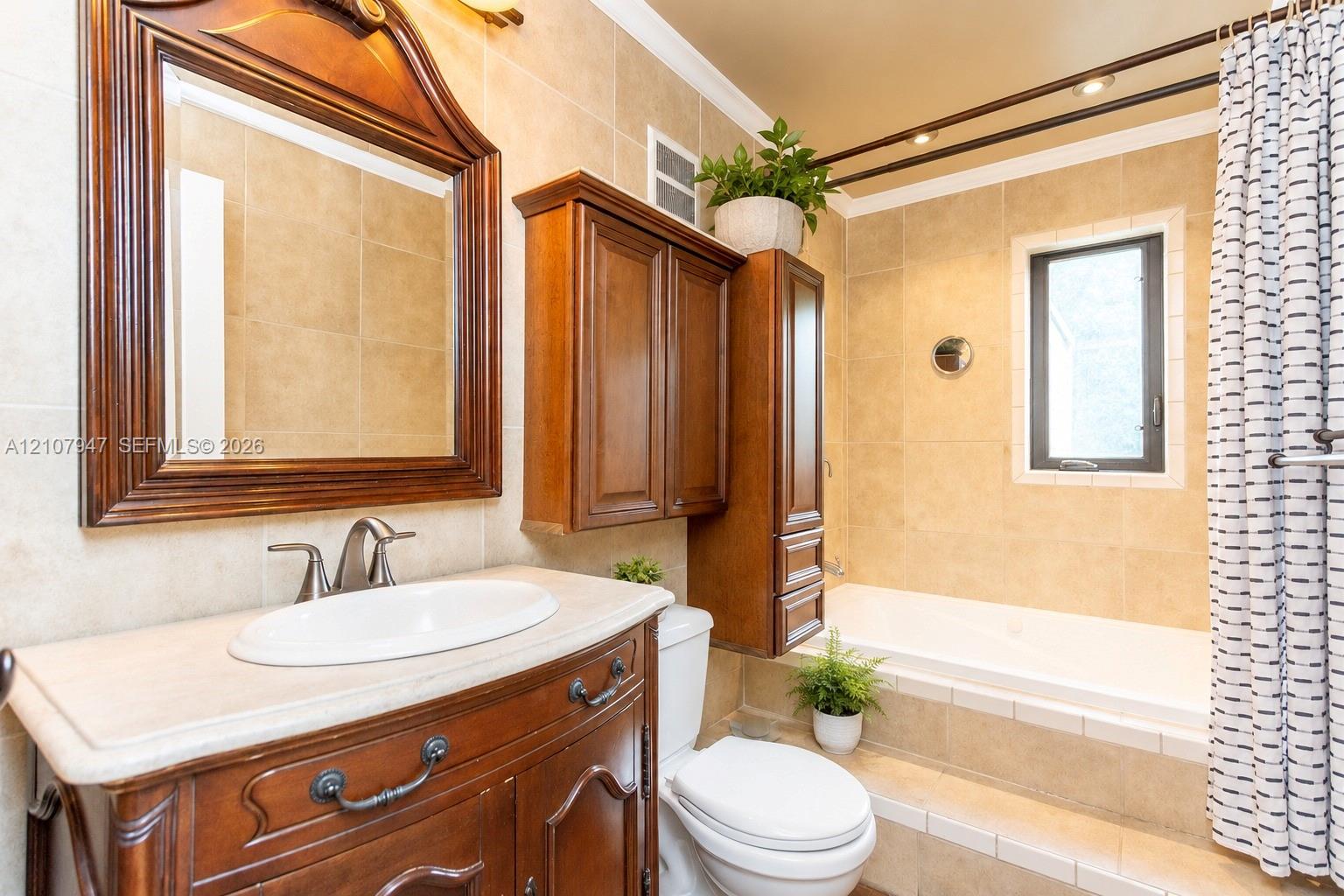 Bathroom featuring a wood vanity with an integrated oval sink and stone-finish countertop, matching wood-frame wall mirror, wall-mounted wood cabinetry, built-in soaking tub with a tile surround, and neutral wall tile throughout Bathroom featuring a wood vanity with an integrated oval sink and stone-finish countertop, matching wood-frame wall mirror, wall-mounted wood cabinetry, built-in soaking tub with a tile surround, and neutral wall tile throughout