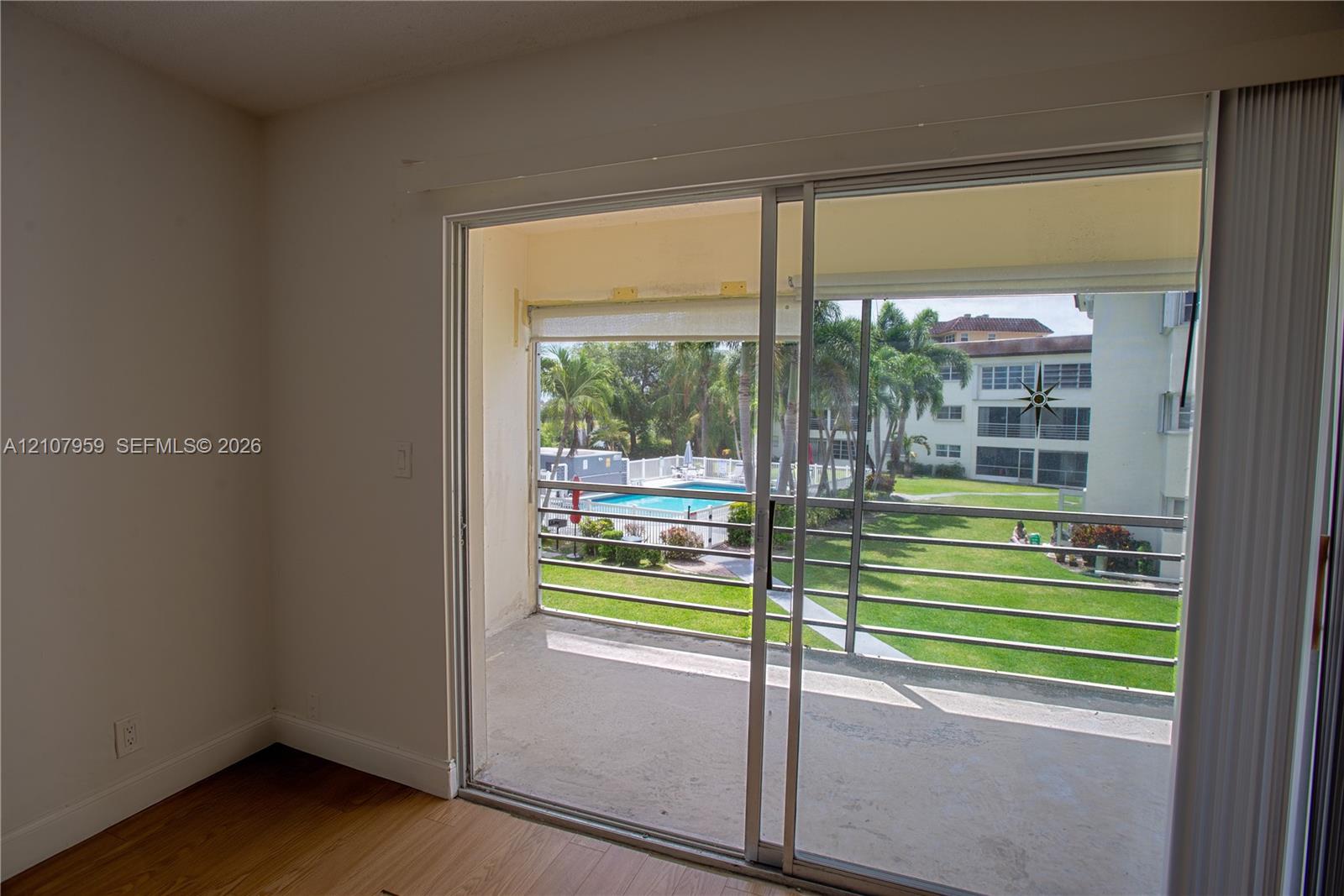 Sliding glass door opening to a private balcony featuring metal railings, wood-finish flooring, and exterior exposure to a swimming pool and landscaped grounds