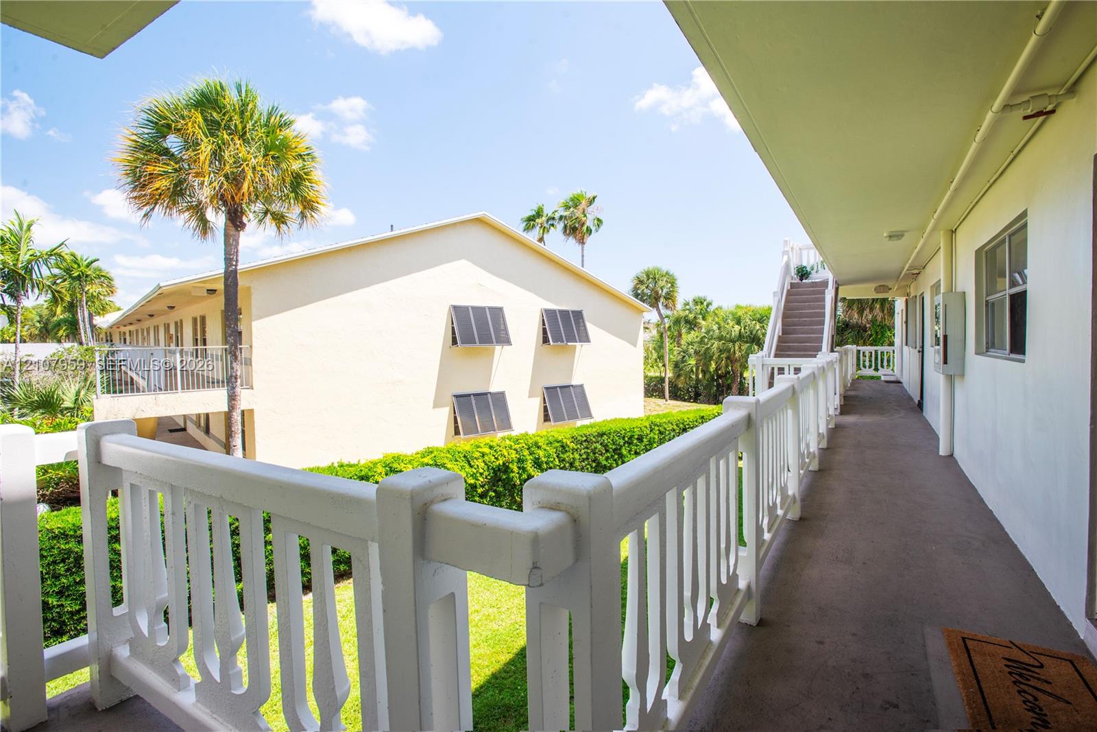 Exterior walkway featuring a white decorative balustrade, paved flooring, and stairwell access