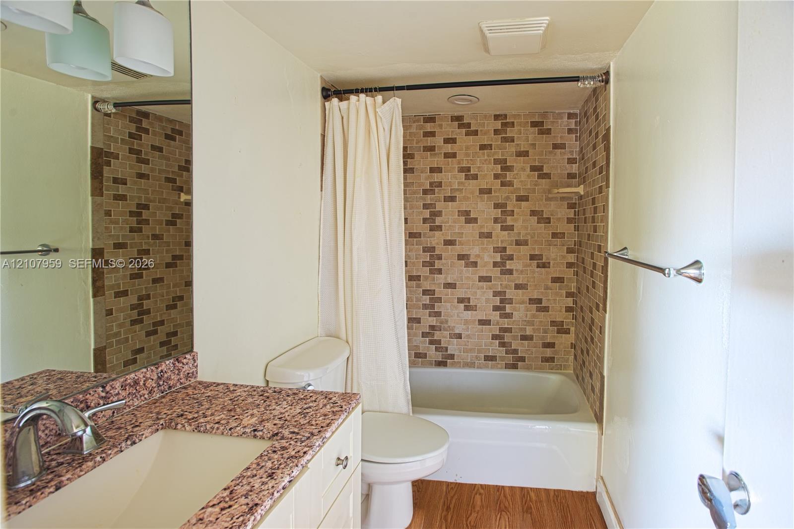 Bathroom featuring a vanity with a stone-finish countertop, undermount sink, multi-tonal tile shower surround, and wood-finish flooring