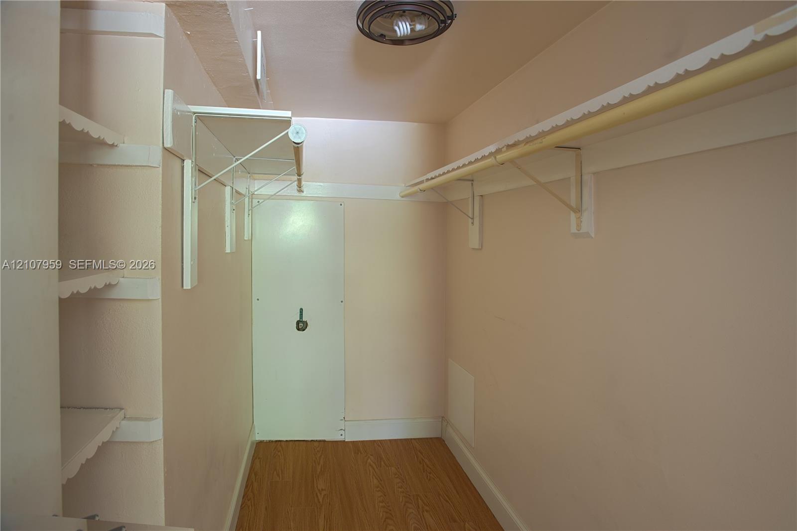 Storage space featuring wood-finish flooring, white shelving units, a hanging rod, and a ceiling-mounted light fixture