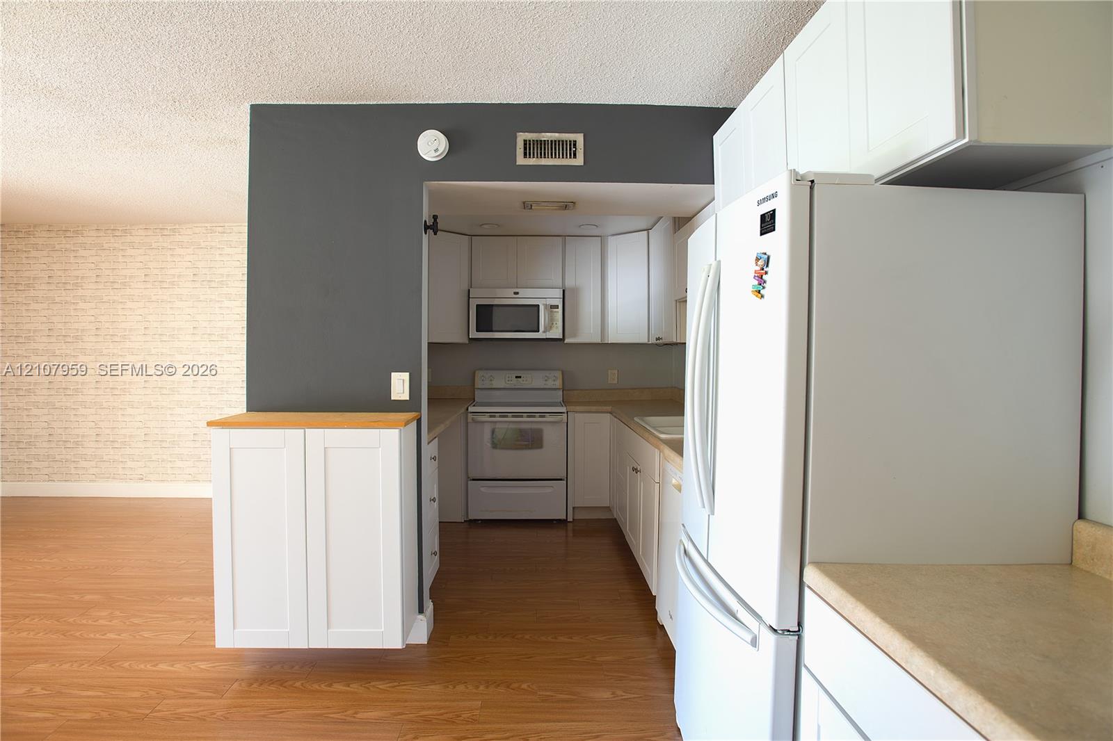 Kitchen area featuring white shaker-style cabinetry, wood-finish flooring, a built-in microwave, and a range