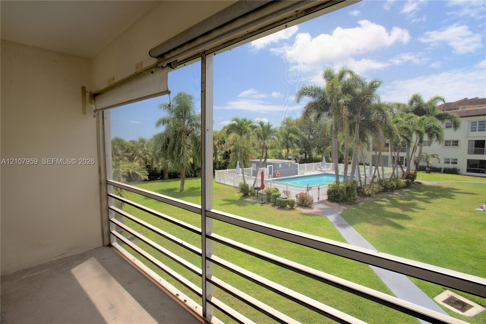 Screened-in balcony featuring metal railing, outdoor pool, paved walkway, and landscaped grounds