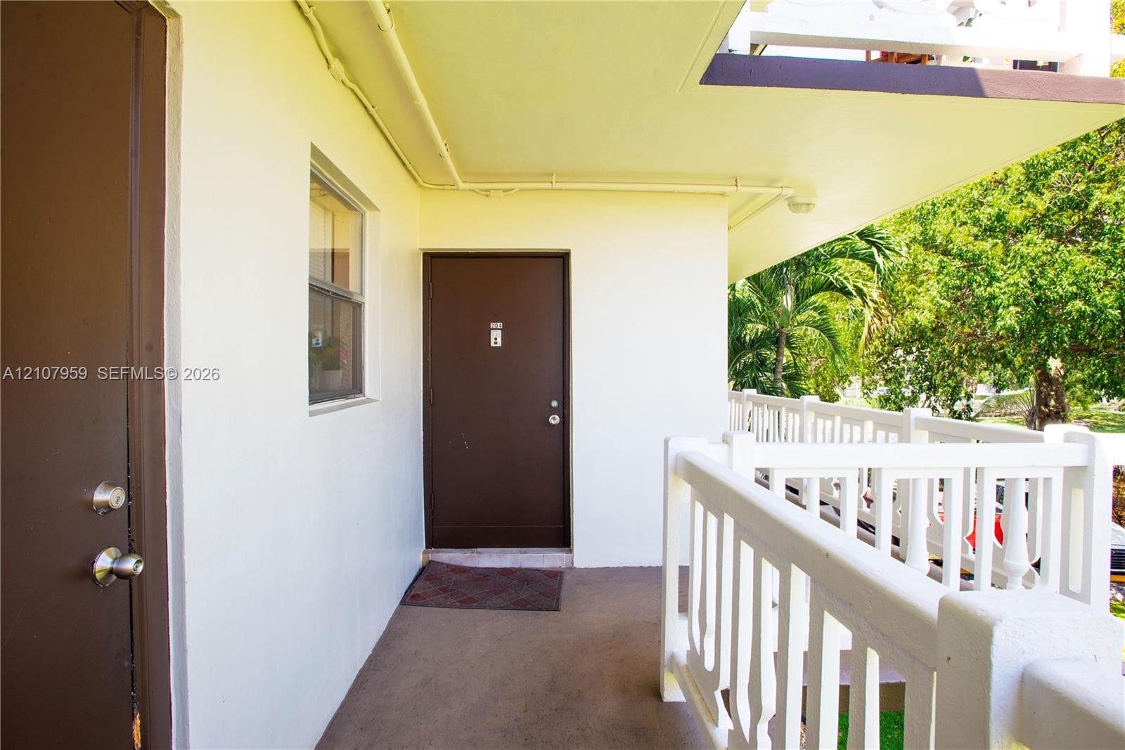 Covered exterior walkway featuring a concrete floor, solid-core doors with metallic hardware, and a white balustrade railing