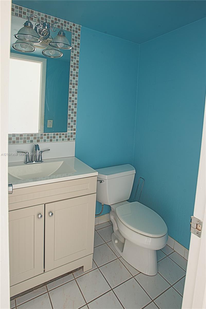 Bathroom featuring a vanity with integrated sink, chrome dual-handle faucet, mosaic tile mirror border, and ceramic tile flooring