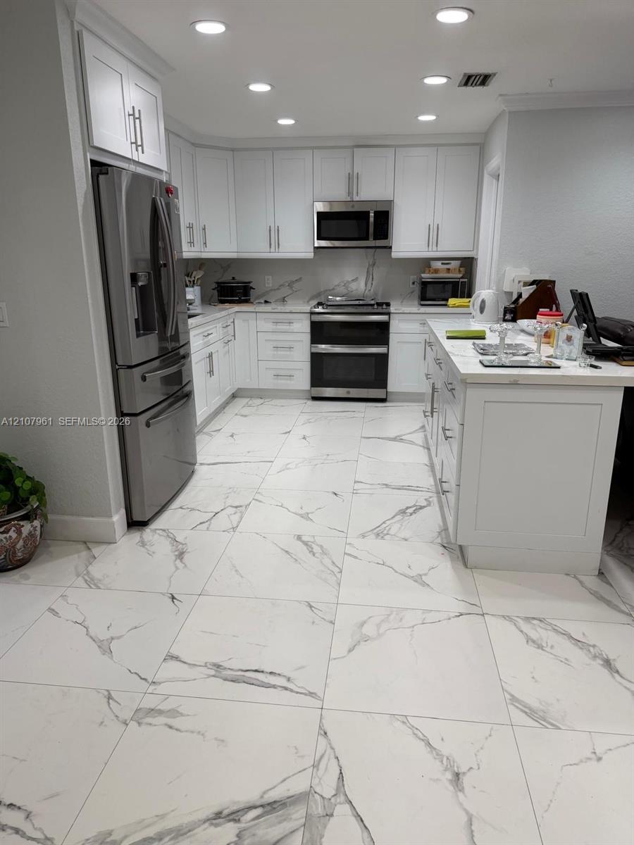 Kitchen featuring white shaker-style cabinetry, stainless steel appliances, a central island with a stone-finish countertop, and large-format tile flooring with a veined pattern