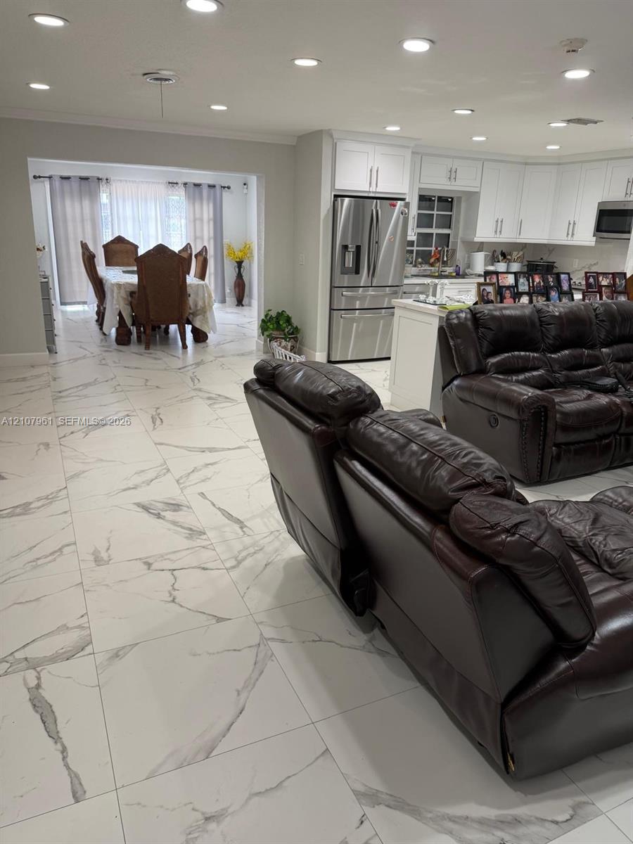 Large-format white tile flooring with grey veining, recessed lighting, white cabinetry, and stainless-steel appliances