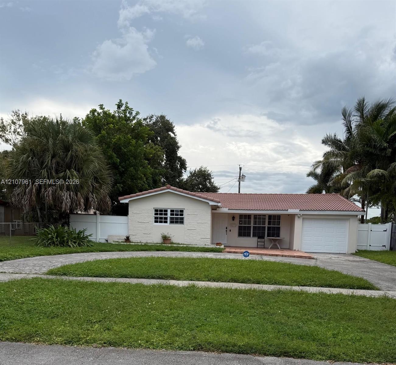 Single-story residence featuring a tile roof, stucco exterior, attached garage, and white vinyl privacy fencing