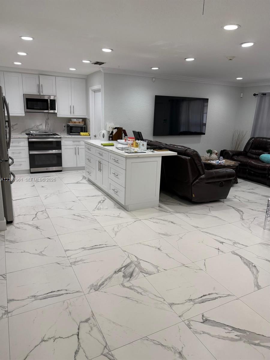 Open-concept kitchen featuring white shaker-style cabinetry, stainless steel appliances, a central island, and large-format tile flooring with stone-pattern veining, finished with recessed lighting