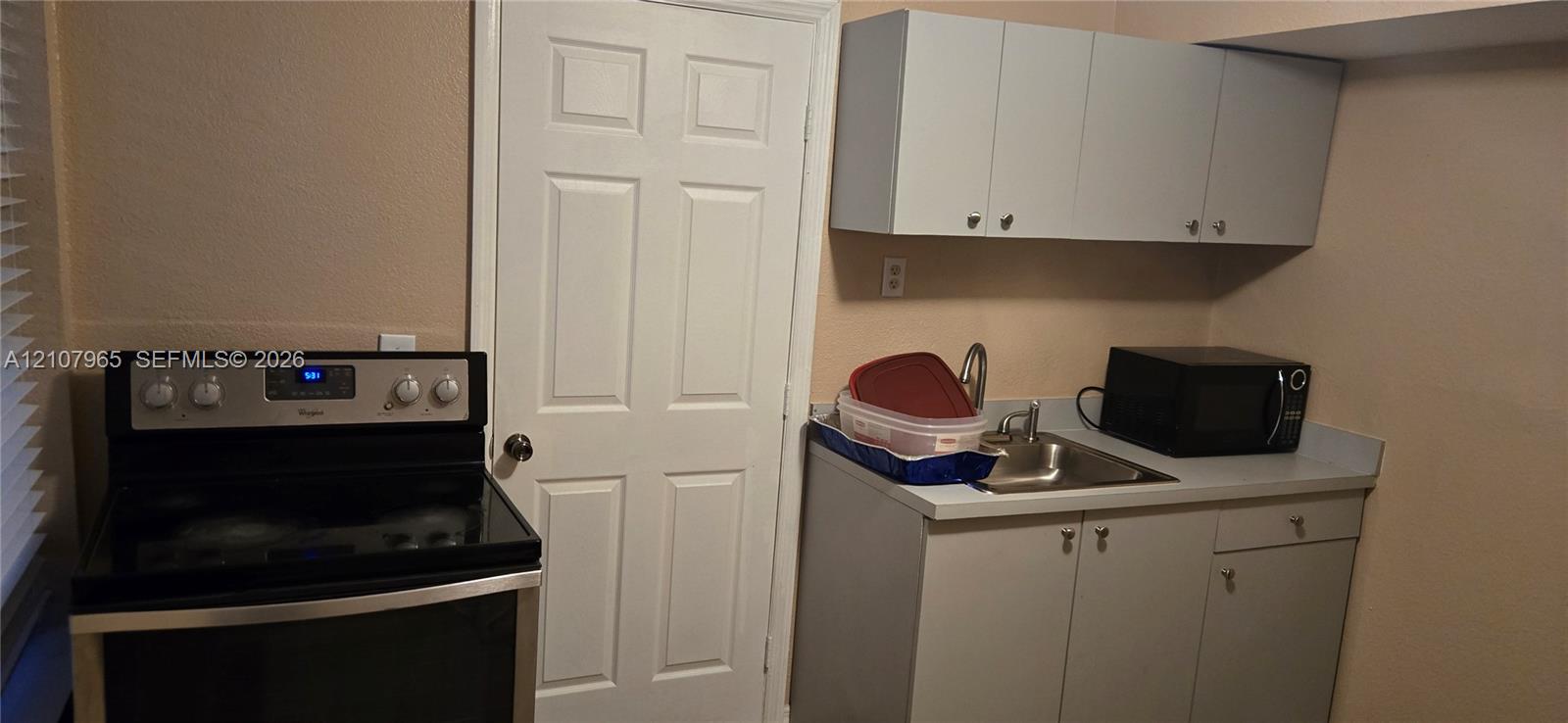 Kitchen area featuring a stainless steel electric range, flat-panel cabinetry, solid-surface countertop, and an integrated stainless steel sink with a gooseneck faucet