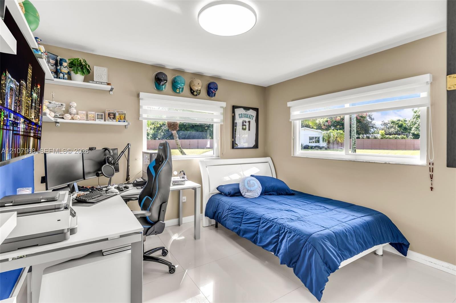 Bedroom featuring glossy tile flooring, neutral wall tones, dual horizontal windows with roller shades, built-in white shelving, and a flush-mount circular ceiling light fixture