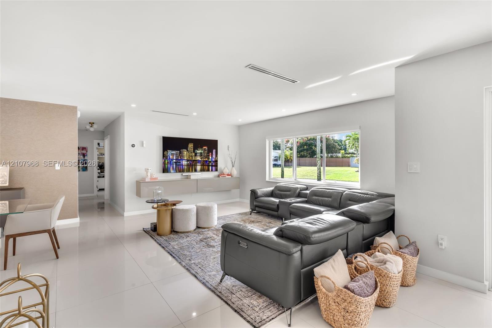 Open-concept interior featuring large-format tile flooring, a wall-mounted floating media console, recessed lighting, and expansive windows