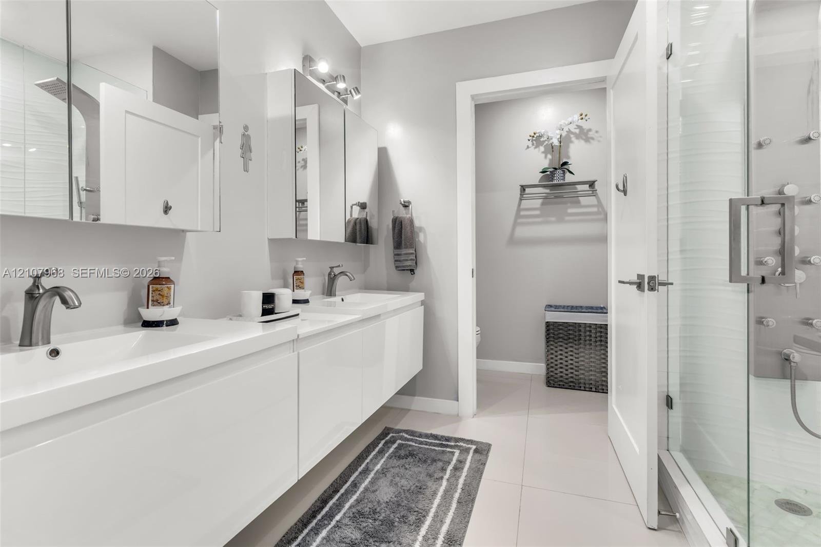 Dual-sink floating vanity with white cabinetry, integrated rectangular basins, and brushed-nickel faucets, complemented by a walk-in glass shower featuring multiple body spray jets and a tiled floor