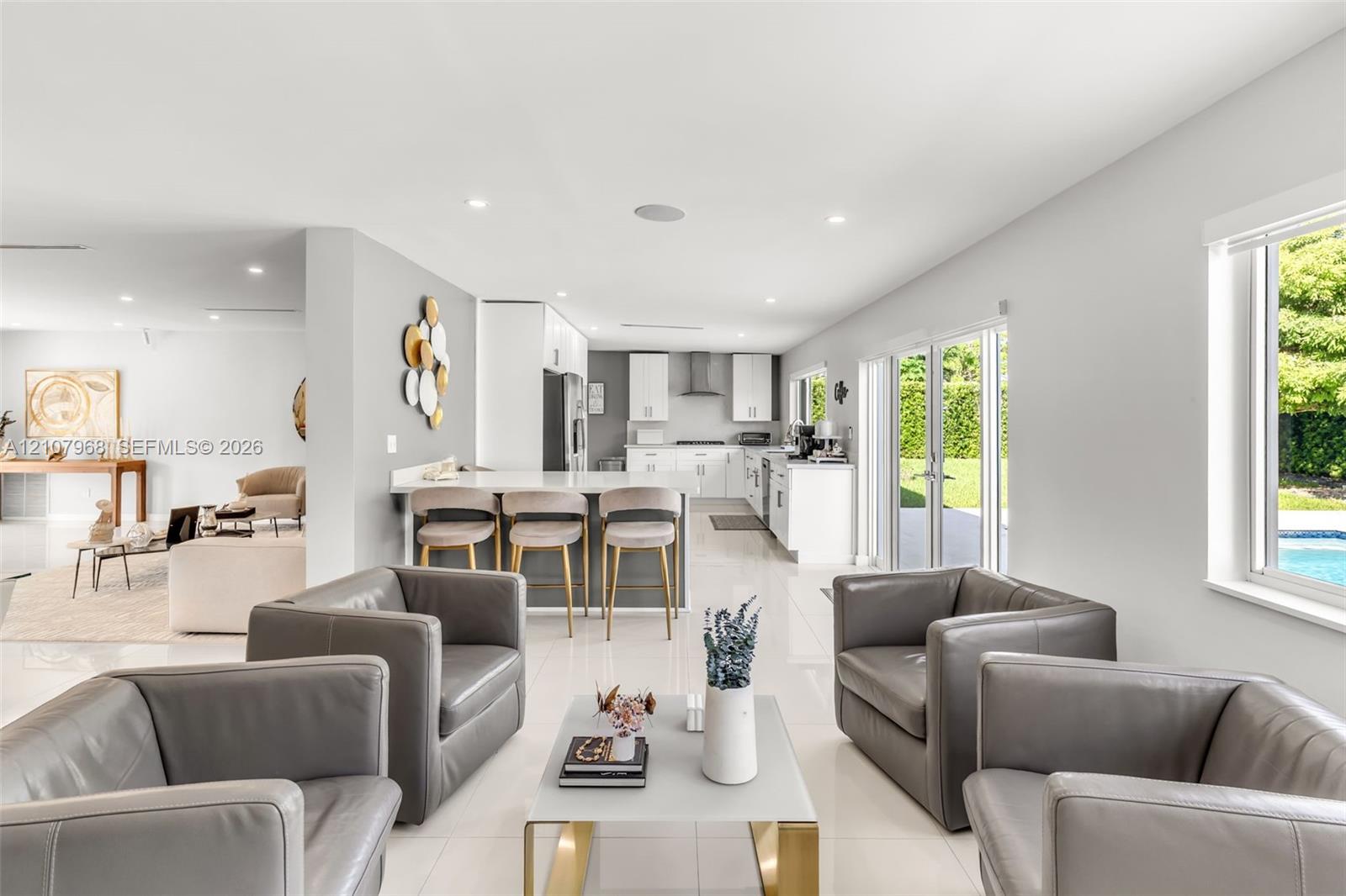 Open-concept kitchen featuring white cabinetry, quartz countertops, a breakfast bar, recessed lighting, and large-format tile flooring