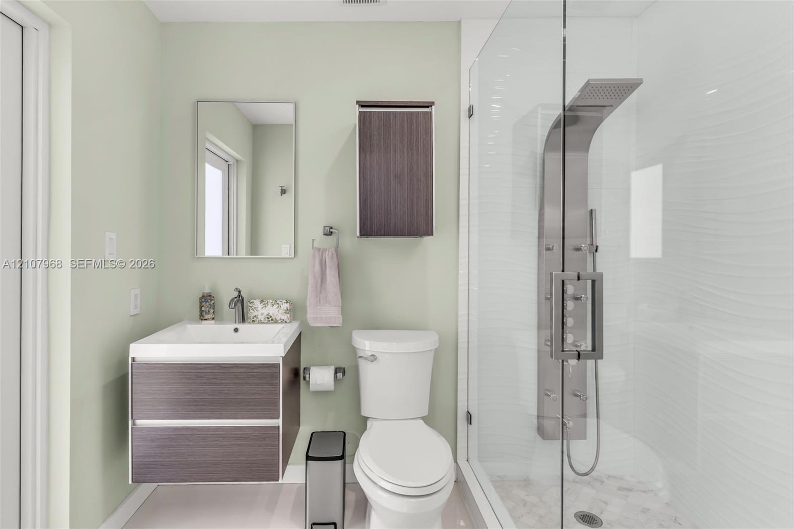 Floating vanity featuring a square vessel sink, integrated wood-finish cabinetry, shower enclosure with a stainless steel rainfall panel system, and a wall-mounted wood-finish storage cabinet