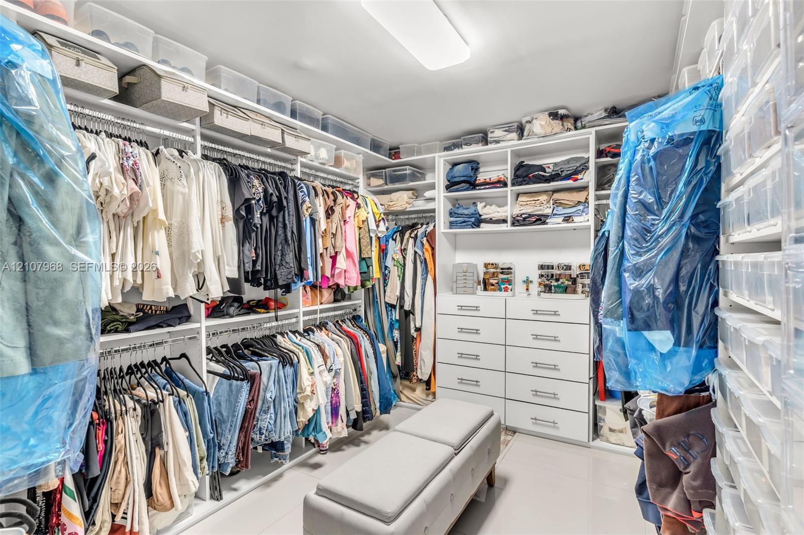 Custom walk-in closet featuring extensive white built-in shelving, integrated dresser drawers with hardware pulls, and overhead lighting