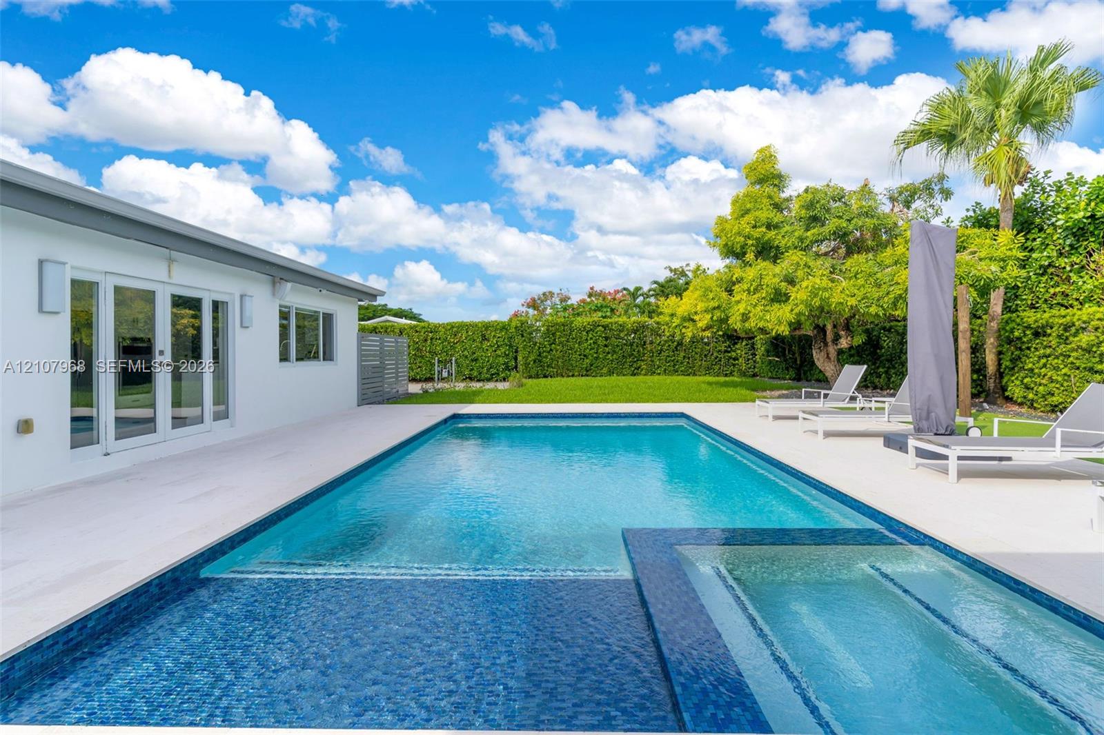 Backyard featuring a custom swimming pool with integrated spa, tile finish, expansive light-toned hardscaping, and privacy hedge