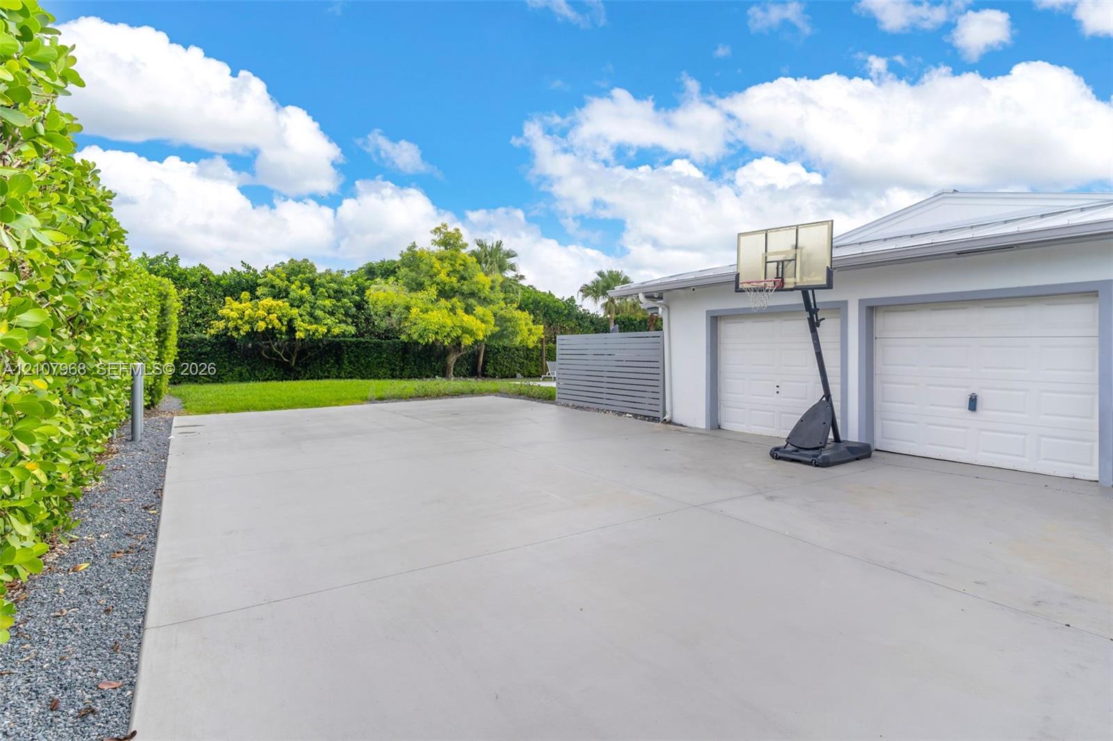 Concrete driveway with two-car garage, manicured lawn, and perimeter privacy hedges