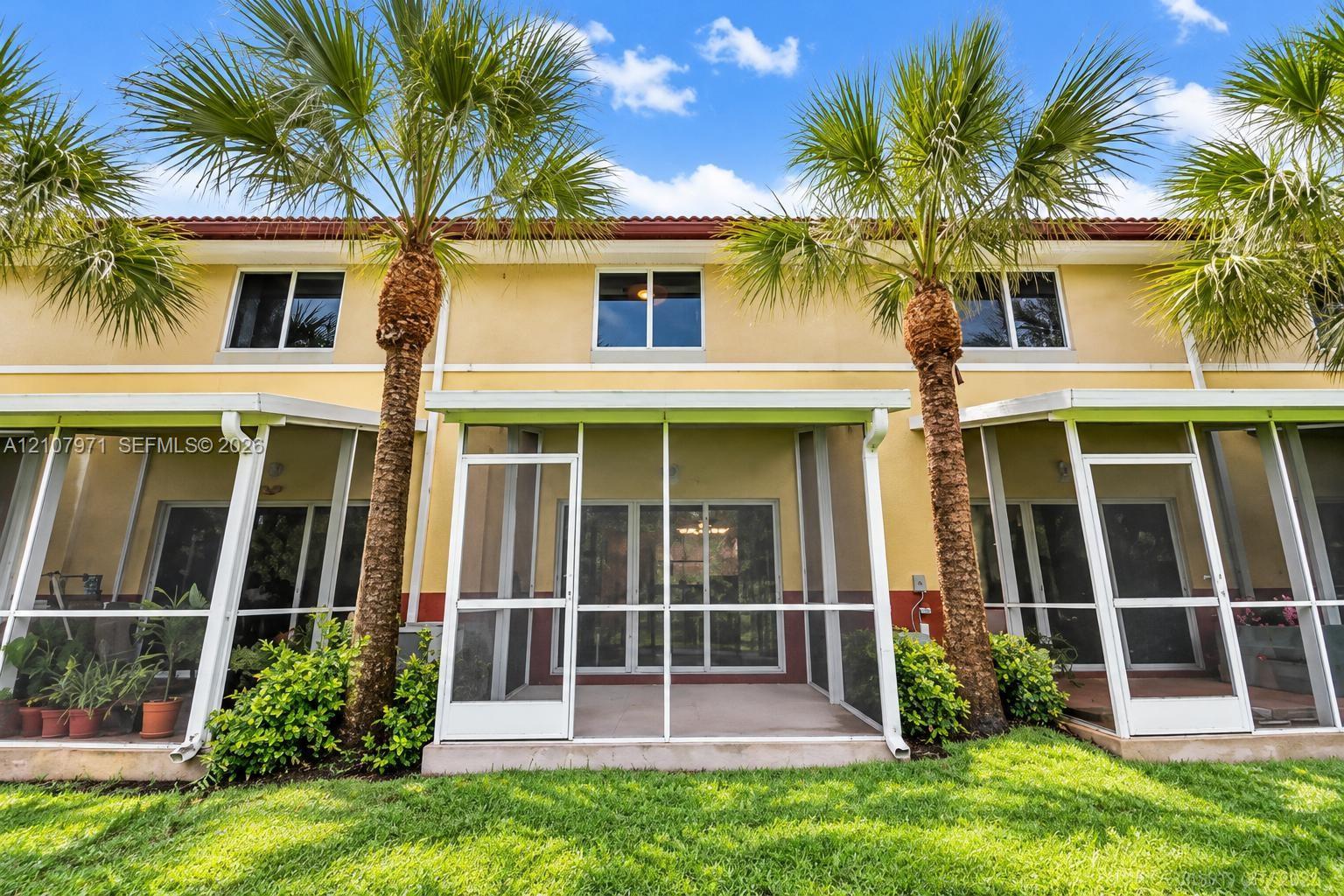 Stucco exterior featuring multiple screened-in lanais, concrete patio flooring, and mature palm trees