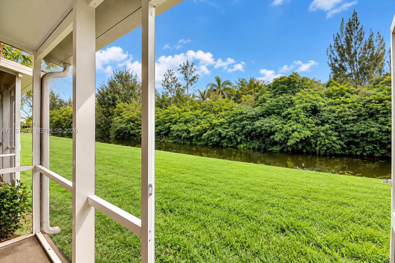 Screened-in porch featuring white structural framing, expansive lawn, mature tree line, and water frontage Screened-in porch featuring white structural framing, expansive lawn, mature tree line, and water frontage