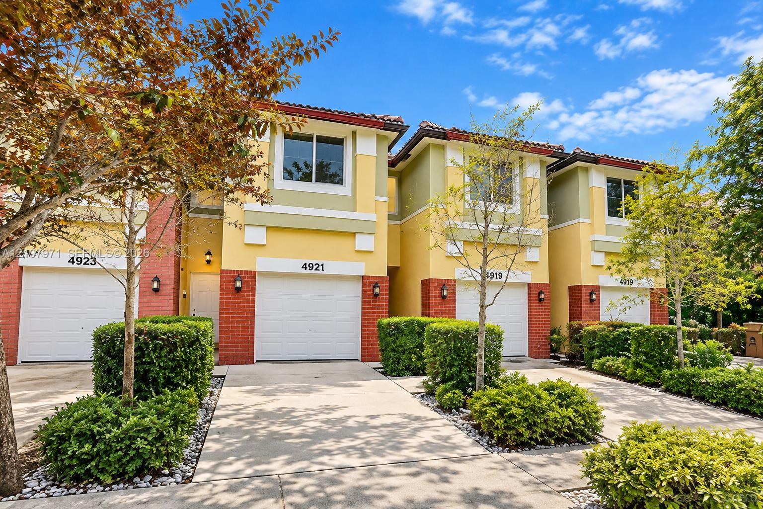 Multi-unit residential exterior featuring a multi-toned stucco facade, brick lower-level detailing, multi-pane windows, and individual garage access