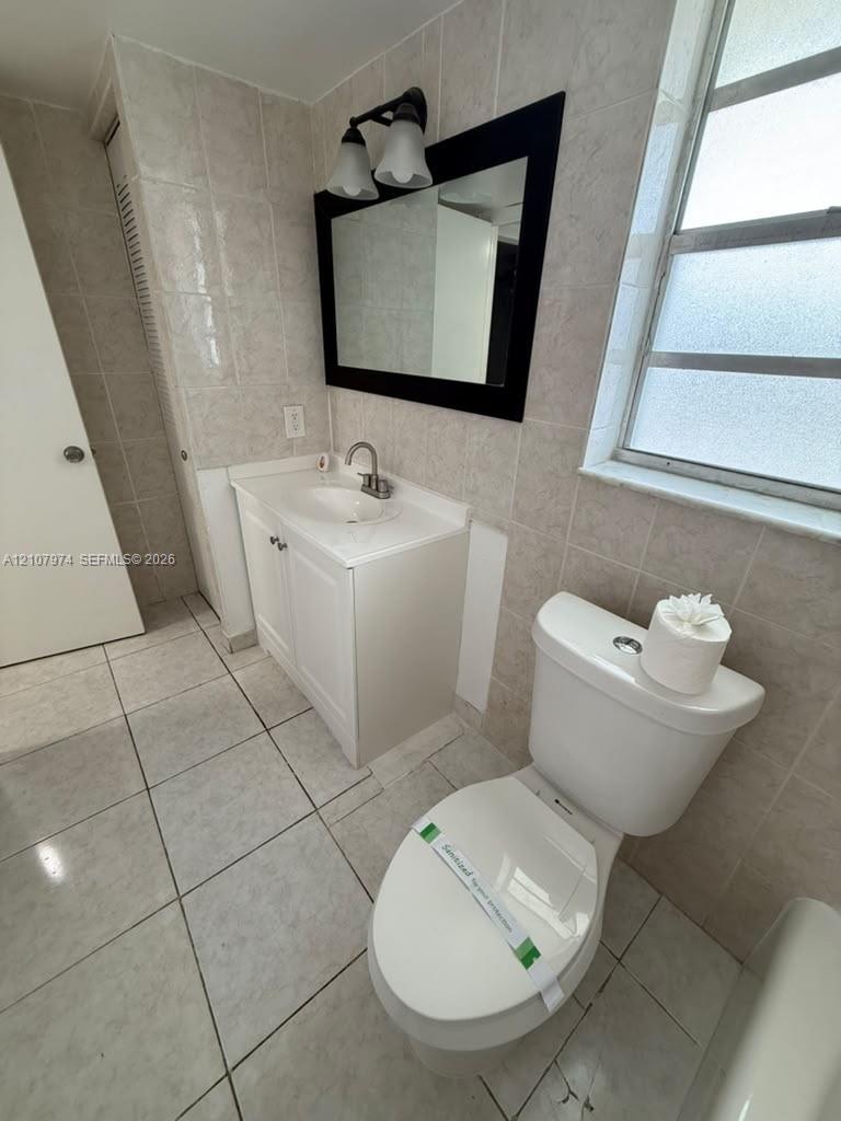 Bathroom featuring floor-to-ceiling tile work, a white vanity with an integrated basin, a framed mirror, and a window with frosted glass