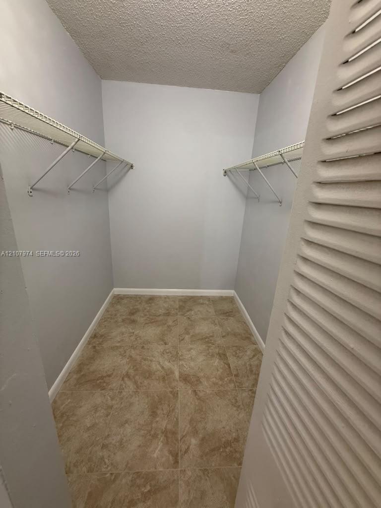 Storage area featuring white wire shelving units, neutral-toned square tile flooring, and louvered door access