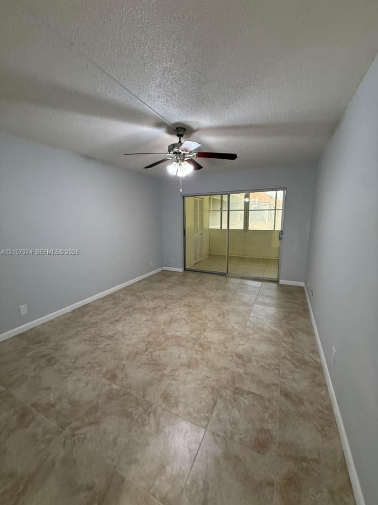 Neutral-toned room featuring stone-finish floor tiling, a ceiling fan with integrated lighting, and sliding glass doors opening to an enclosed space