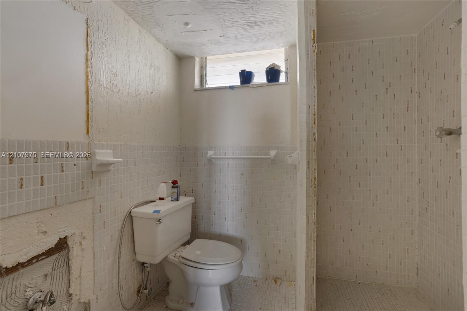 Bathroom featuring square white wall tiling, a built-in shower enclosure, a white porcelain toilet, and a recessed window