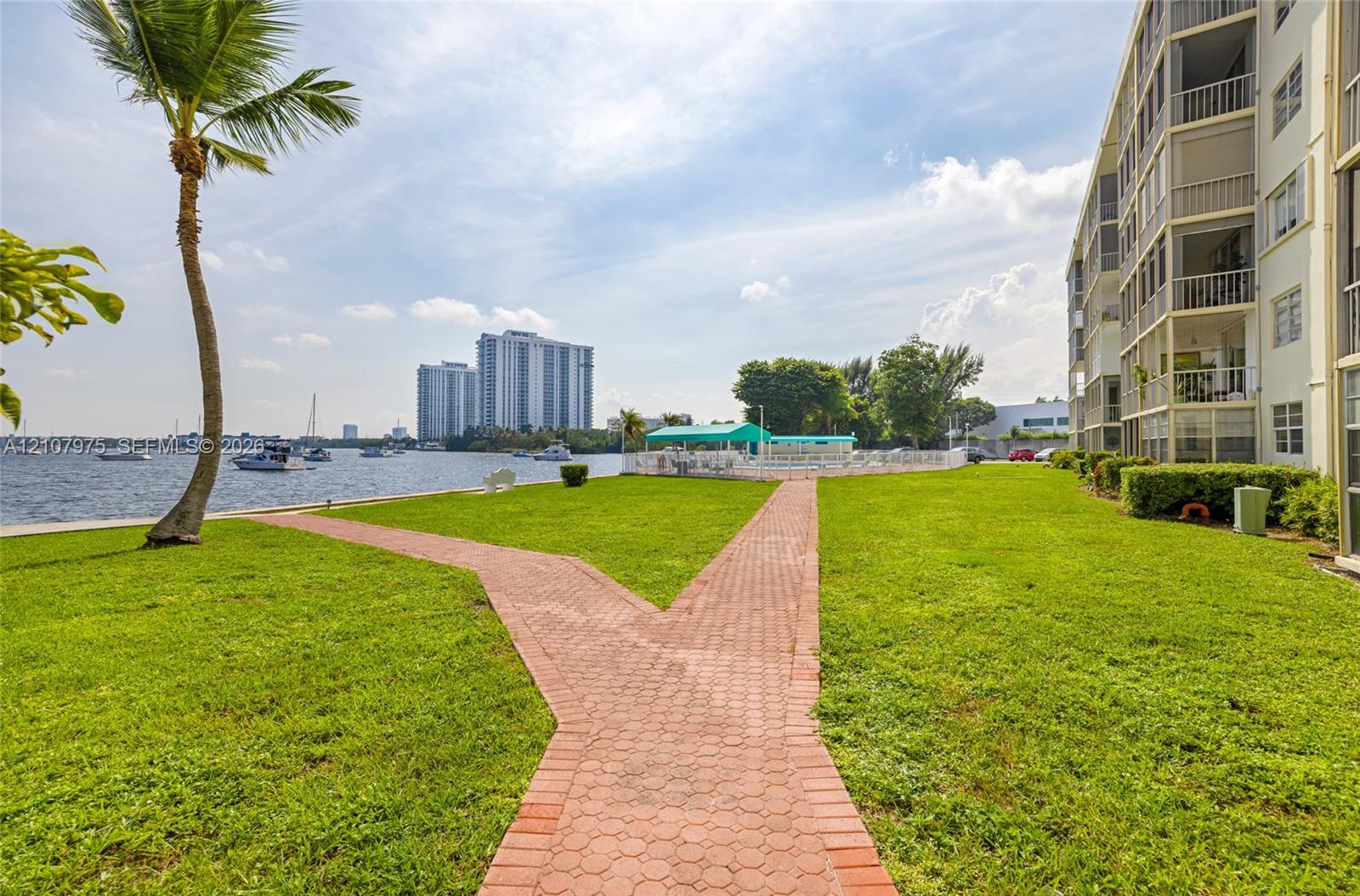 Waterfront grounds featuring manicured lawn, brick paver pathway, and exterior balcony structures