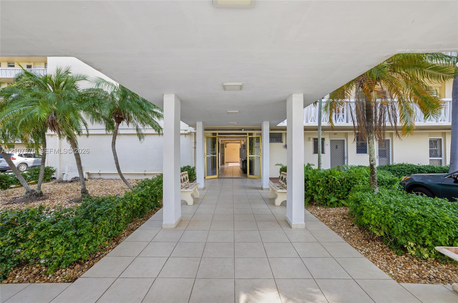 Covered entrance featuring large-format ceramic floor tiles, square support pillars, integrated ceiling lighting, and flanking landscaping